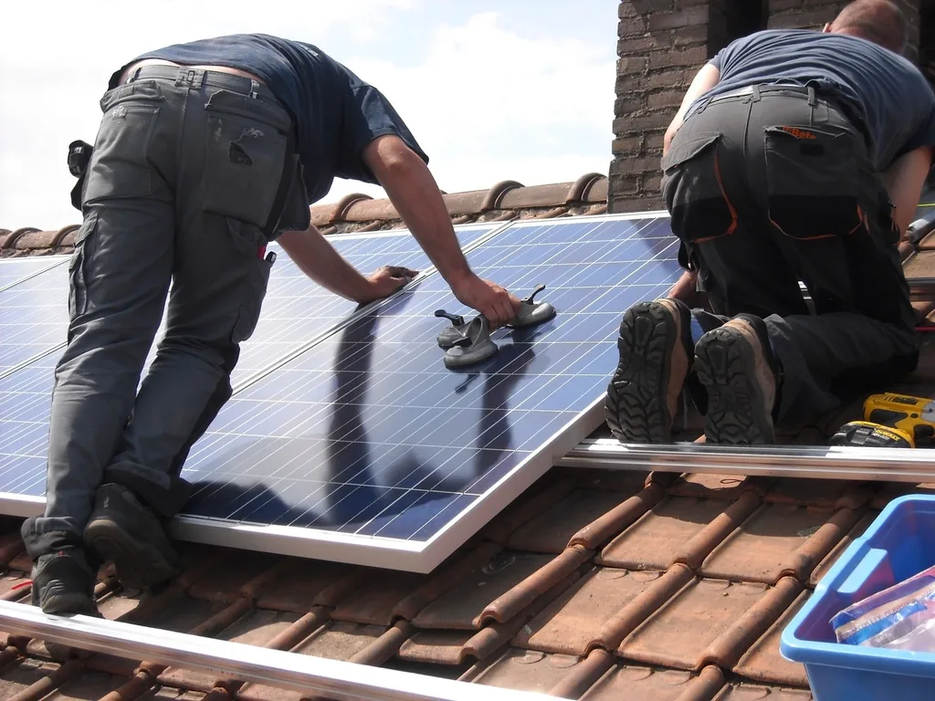Twee monteurs leggen zonnepanelen op een pannendak, met gereedschap naast zich.